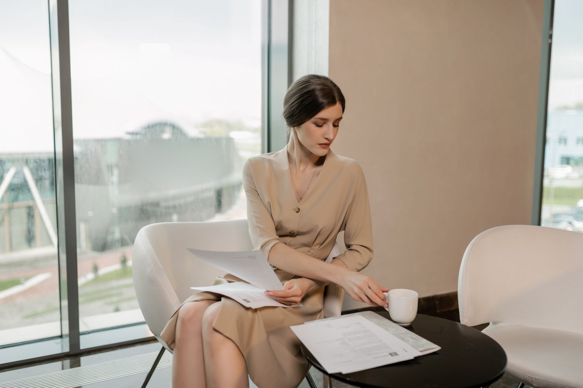 Professional woman examining documents while enjoying coffee in a modern office setting.